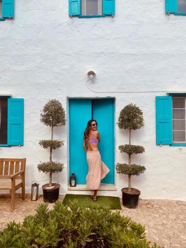 a woman in a dress standing in front of a blue door at Habitaciones Casa de Campo Daymipaz in Mahón