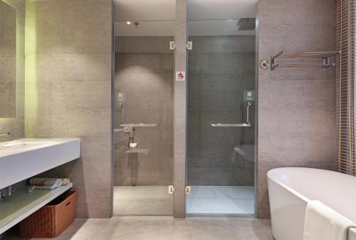 a bathroom with a glass shower with a tub and a sink at Haikou Meilan International Airport Hotel in Haikou