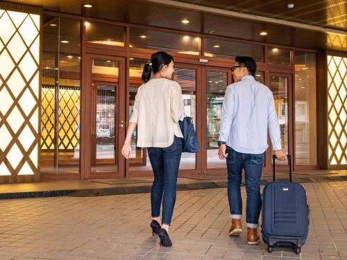 a man and woman walking down a street with a suitcase at Hotel Flags Isahaya Nagasaki in Isahaya
