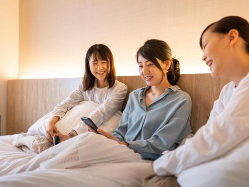 a group of three women sitting on a bed at Hotel Flags Isahaya Nagasaki in Isahaya