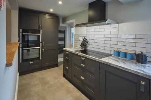 a kitchen with black cabinets and a white brick wall at Host & Stay - Arncliffe View in Egton