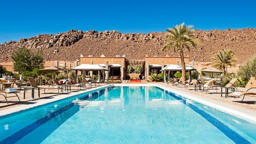 a swimming pool with chairs and a mountain in the background at HOTEL Bab Rimal in Foum Zguid