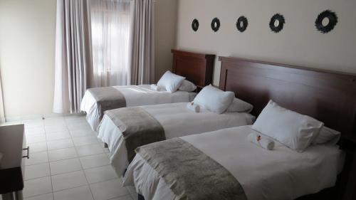 Una habitación de hotel con tres camas con sábanas blancas. en Villa Strada Guesthouse, en Klerksdorp