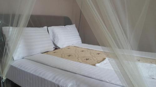 a bed with white sheets and pillows and a curtain at Blue Dove Koboko in Koboko