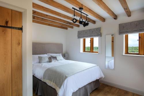 a bedroom with a bed with white sheets and windows at Hastings Retreat Rural barn conversions with Private Lake in Ashby de la Zouch