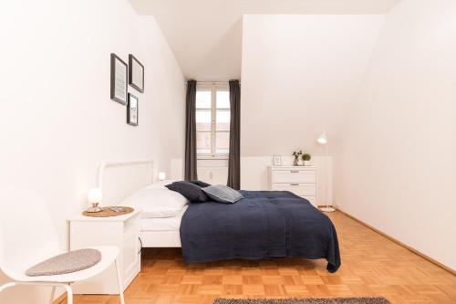 a white bedroom with a bed and a chair at Cozy Kunsthaus GRAZ in Graz
