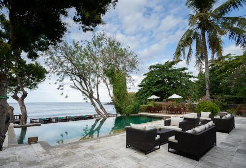 a pool with couches and chairs next to the ocean at Mimpi Resort Tulamben in Tulamben