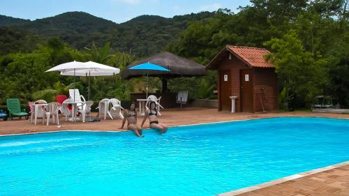 two people jumping into a swimming pool at Pousada Salve Floresta in Tapiraí