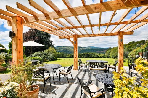 a patio with tables and chairs under a wooden pergola at The Horn Of Plenty in Tavistock