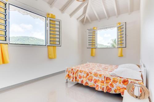 a bedroom with two windows and a bed in it at Le Colibri Vert in Le Morne-Vert