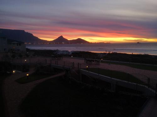 a sunset over the beach with a mountain in the distance at Lagoon Beach Neptune Isle Cape Town in Cape Town