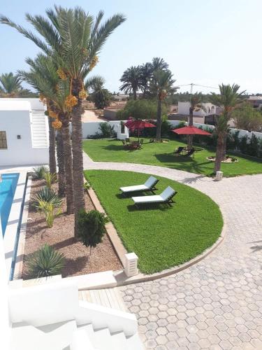 a resort with a pool and palm trees and benches at Dar El Jerbi in Mezraya