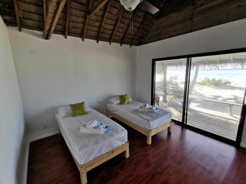 2 Betten in einem Zimmer mit einem großen Fenster in der Unterkunft AOTERA GUEST HOUSE in Avatoru