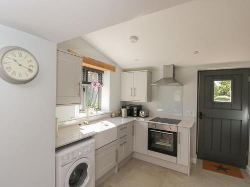 a kitchen with white cabinets and a clock on the wall at Kingfisher, 2 The Old Stables in Witney