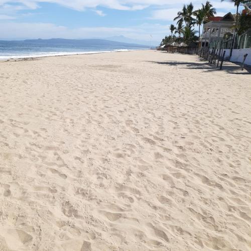 a sandy beach with palm trees and the ocean at Bungalows Maria Teresa in Rincon de Guayabitos