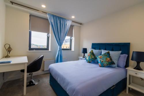 um quarto com uma cama azul, uma secretária e uma janela. em Virexxa Bedford Centre - Supreme Suite - 2Bed Flat with Free Parking & Gym em Bedford