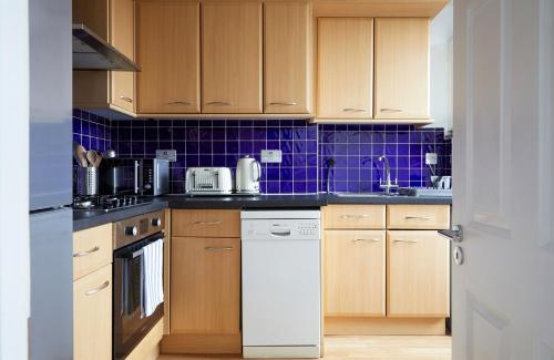 cocina con armarios de madera y lavavajillas blanco en FW Haute Apartments at North Finchley, a 3 Bedroom and 2 Bathroom Pet-Friendly Flat, King or Twin beds with FREE WIFI, en Finchley