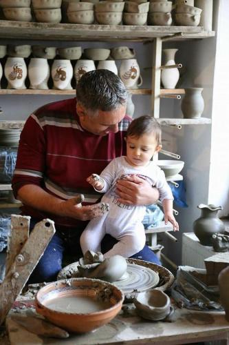 a man holding a baby sitting on a table with pottery at Conacul Paloși in Horezu
