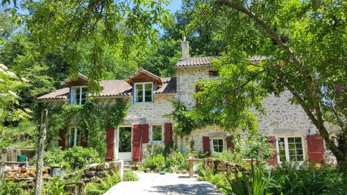 a stone house with red shutters and trees at Le Moulin de Pensol in Pensol