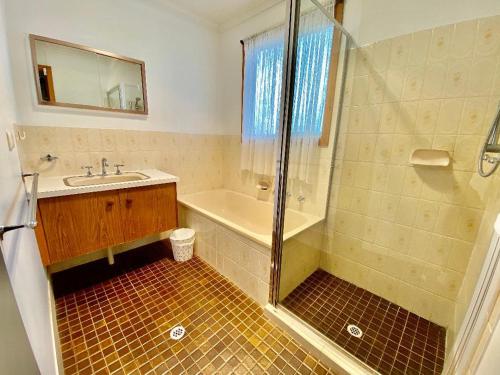 bagno con vasca, lavandino e doccia di Sevens Avenue Guest House a Euroa