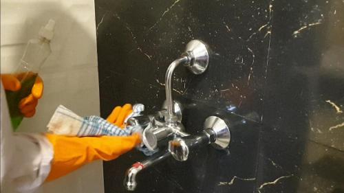 a person in an orange rubber glove manipulating a bathroom faucet at Panthashala Santiniketan in Srī Niketan