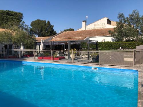 a large blue swimming pool in front of a building at Logis Hôtel Restaurant Les Aubuns in Caissargues