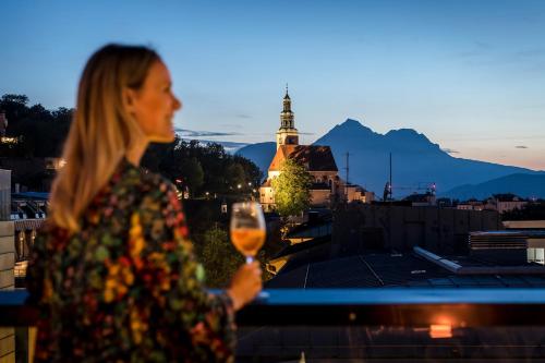 a woman holding a glass of wine overlooking a city at IMLAUER HOTEL PITTER Salzburg in Salzburg