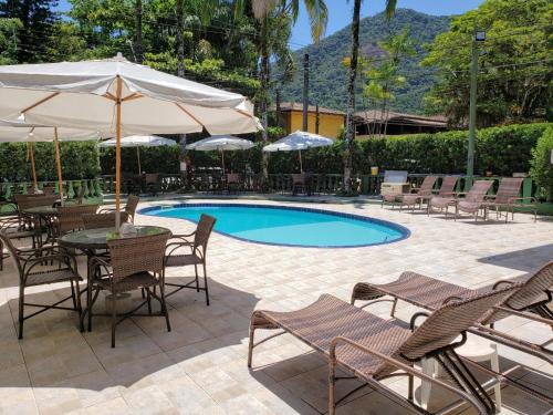 a pool with chairs and a table and an umbrella at Pousada Flores do Lázaro in Ubatuba