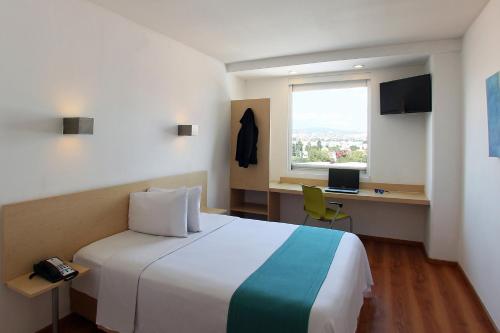 a hotel room with a bed and a desk and a window at One Queretaro Plaza Galerias in Querétaro