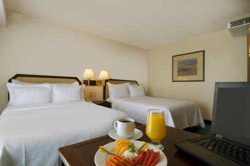 a hotel room with two beds and a table with a plate of food at Fiesta Inn Mexicali in Mexicali