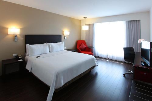 a hotel room with a white bed and a red chair at Fiesta Inn Cuautitlan in Tepotzotlán