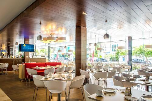a restaurant with white tables and chairs and a large window at Fiesta Inn Playa del Carmen in Playa del Carmen
