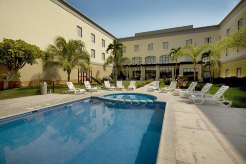 un hôtel avec une piscine, des chaises et un bâtiment dans l'établissement Fiesta Inn Colima, à Colima