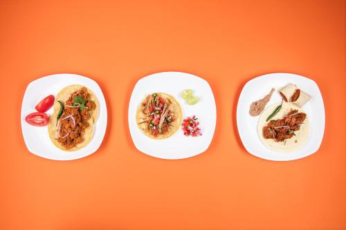 three plates of food on a orange background at One Leon Poliforum in León