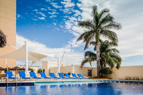 une piscine avec des chaises longues bleues et un palmier dans l'établissement Fiesta Inn Tuxtla Gutierrez, à Tuxtla Gutiérrez