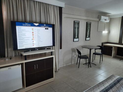 a living room with a television and a table with chairs at Hotel Metrópole Maringá in Maringá