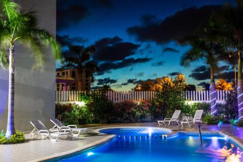 una piscina con sillas y palmeras por la noche en One Cancun Centro, en Cancún