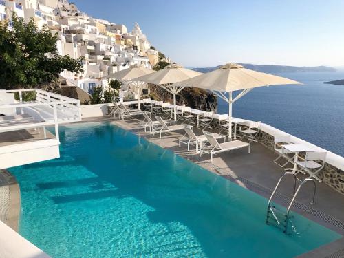 a swimming pool with chairs and umbrellas and the ocean at Panorama Suites in Fira