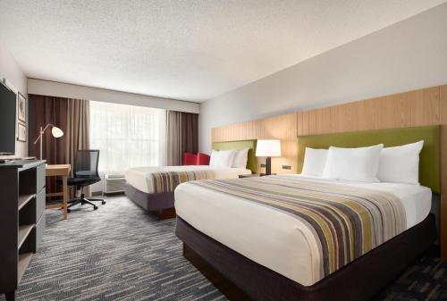 PellaにあるCountry Inn & Suites by Radisson, Pella, IAのベッド2台とデスクが備わるホテルルームです。