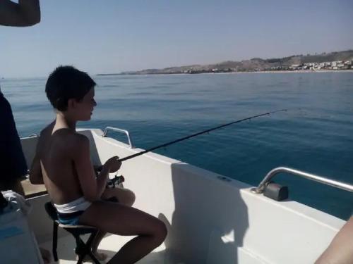 サンタ・カテリーナ・デッロ・イオーニオにあるSanta Caterina dello Ionio Boutique Apartmentsの釣竿を持った舟に腰掛けた少年