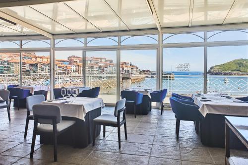 a restaurant with tables and chairs and a view of the ocean at Hotel Silken Palacio Uribarren in Lekeitio
