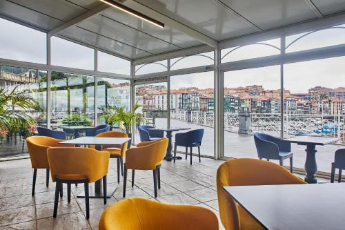 un restaurante con mesas, sillas y ventanas grandes en Hotel Silken Palacio Uribarren, en Lekeitio