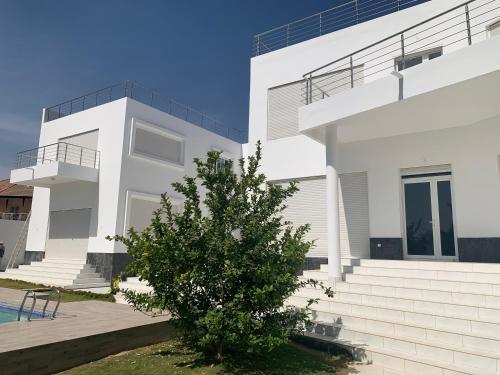 a white house with a tree in front of it at Appartement Luxueux En Résidence vu sur mer à 50 mètres de la plage in Sali Tapé