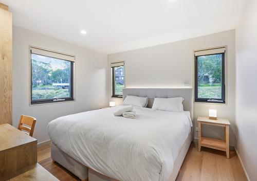 a bedroom with a large white bed with two windows at Blackout in Dinner Plain