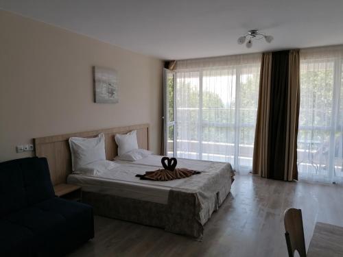 a bedroom with a bed and a chair and windows at Apart Allure Dobi in Primorsko