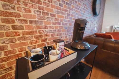 een tafel met kopjes en een koffiezetapparaat op een bakstenen muur bij THE VINTAGE APARTMENT AU COEUR DE LA VILLE DE RIMBAUD in Charleville-Mézières