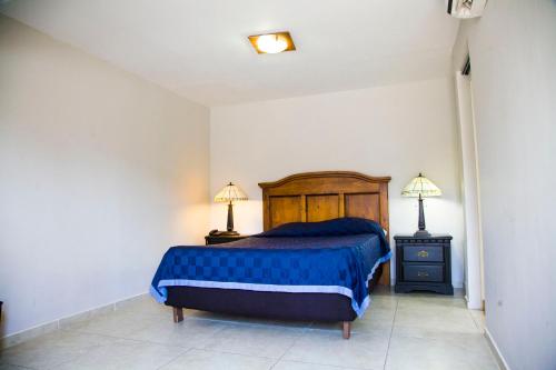a bedroom with a bed with a blue blanket and two lamps at Hotel Cosmos Don Carlos in Mexicali