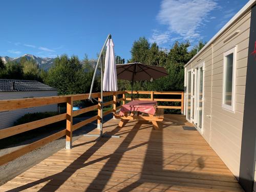 a wooden deck with an umbrella and a bench at Mobilhome 3 étoiles in Embrun