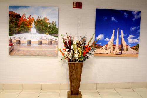 a vase of flowers on a wall with paintings at Baymont by Wyndham Lafayette - Purdue University in Lafayette
