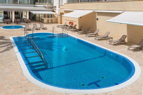 una gran piscina azul con sillas y mesas. en Hotel Biniamar en Cala Millor